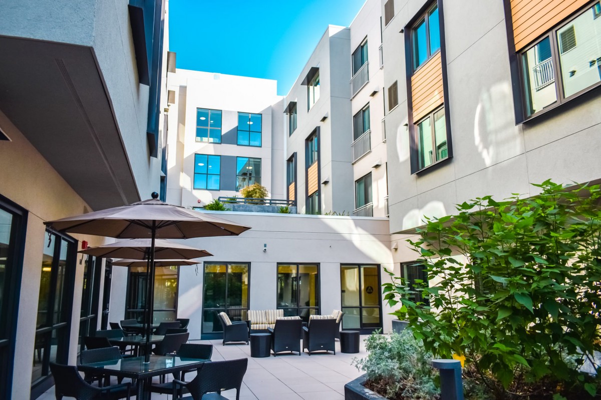 A modern apartment courtyard with outdoor seating and umbrellas under a clear blue sky.