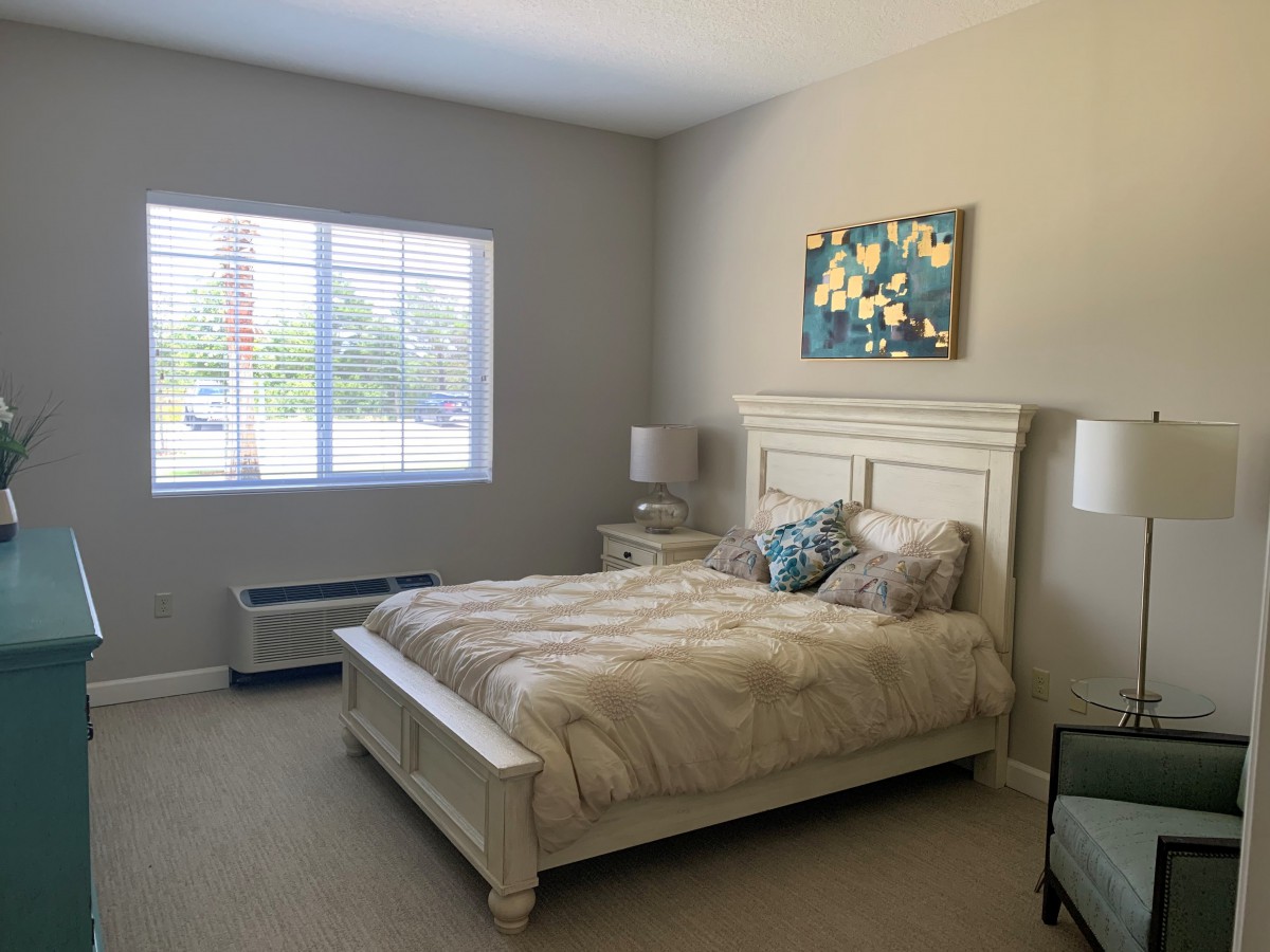 A cozy bedroom with a comfortable bed, soft lighting, and a window with blinds.