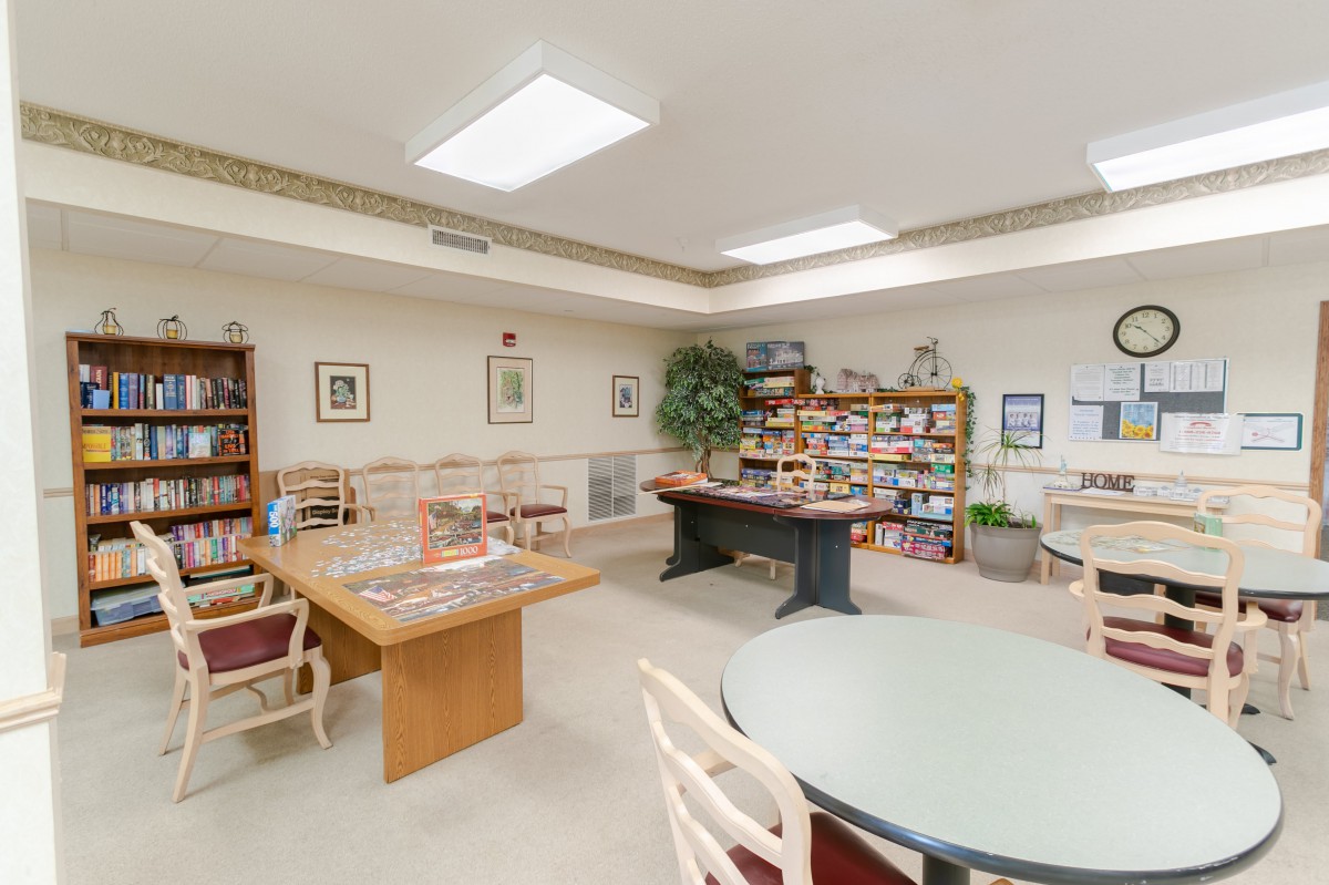 A recreational room with tables, chairs, a foosball table, and shelves filled with games.