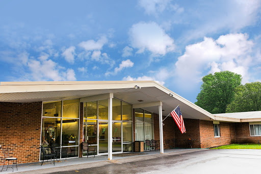 A modern building featuring large glass windows, complemented by an American flag, set against a cloudy sky.