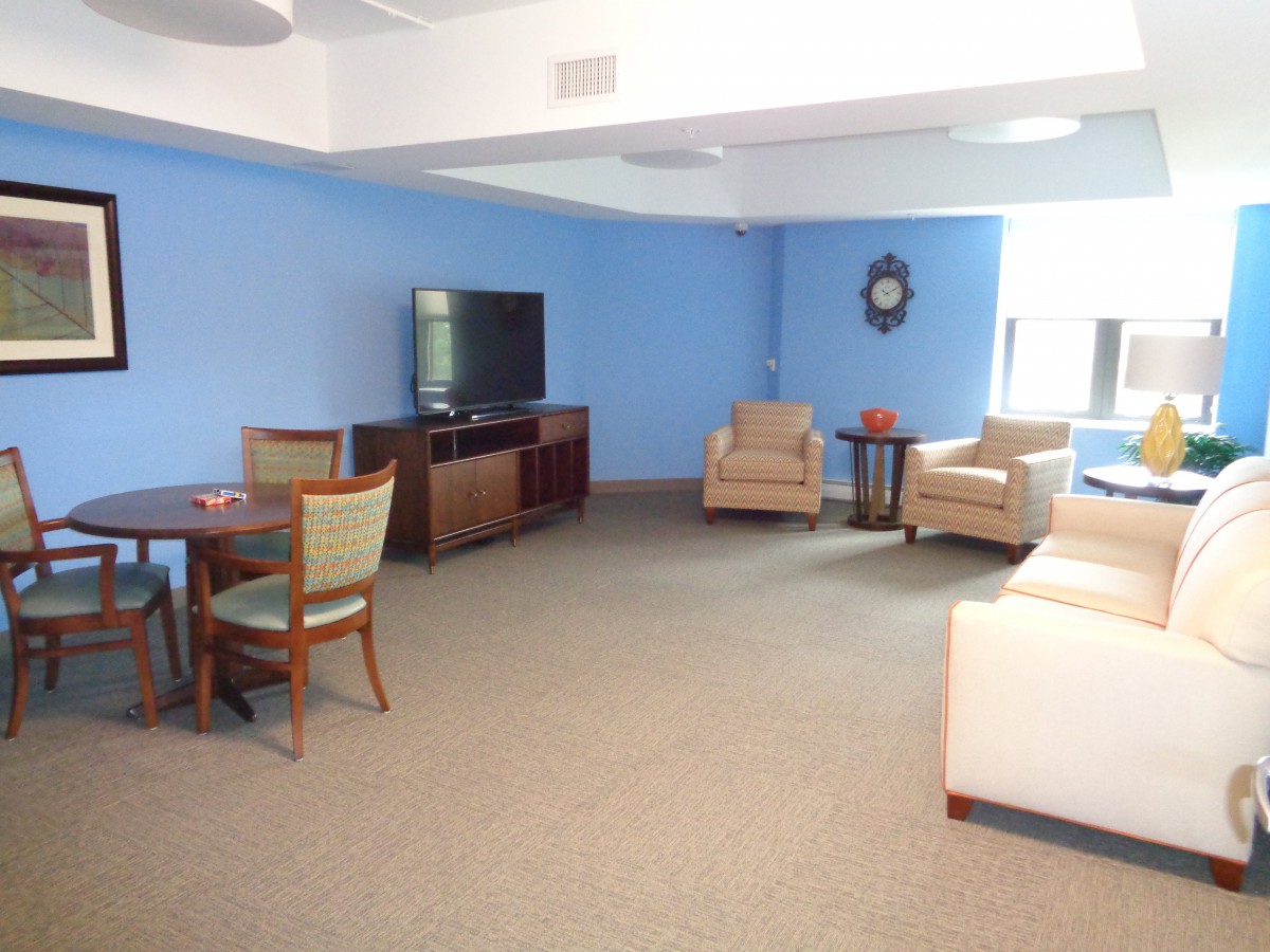 A cozy living room with blue walls, featuring a TV, sofa, chairs, and a table.