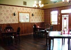 A cozy dining area with wooden tables and chairs, warm lighting, and classic wallpaper.