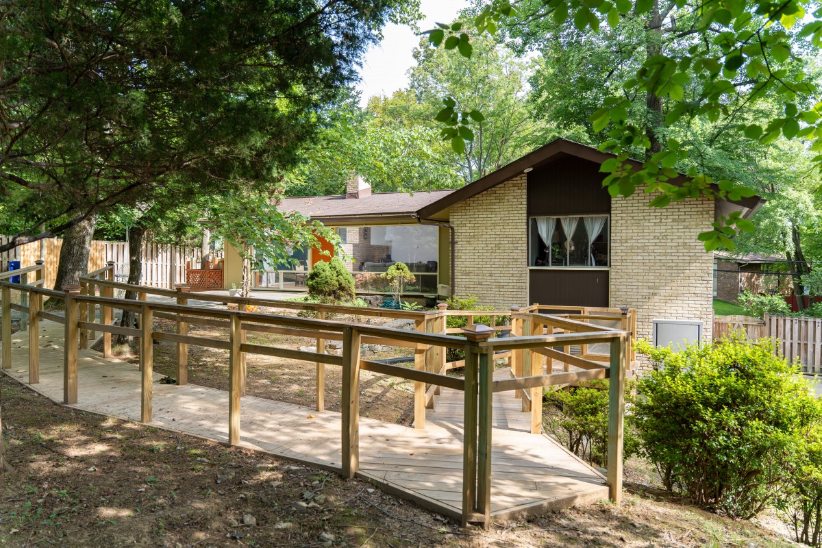 A house surrounded by trees with a wooden ramp leading to the entrance.