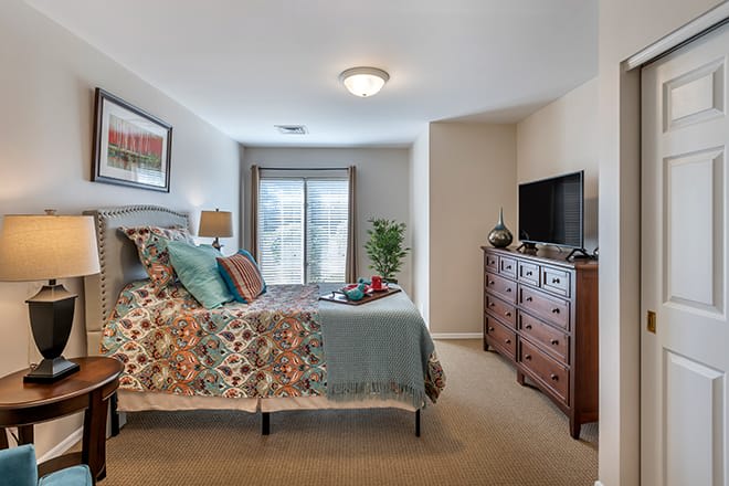 A cozy and well-decorated bedroom with a bed, dresser, and television.