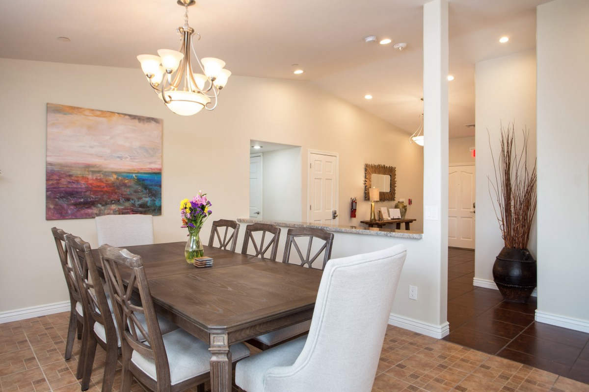 A modern dining room featuring a wooden table with elegant chairs, enhanced by a chandelier and vibrant artwork.