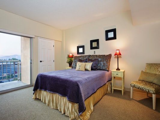 A cozy bedroom with a neatly made bed, accented by decorative pillows and nightstands with lamps.
