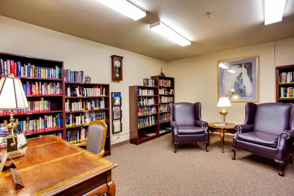 A cozy library reading room with bookshelves, armchairs, and a lamp.