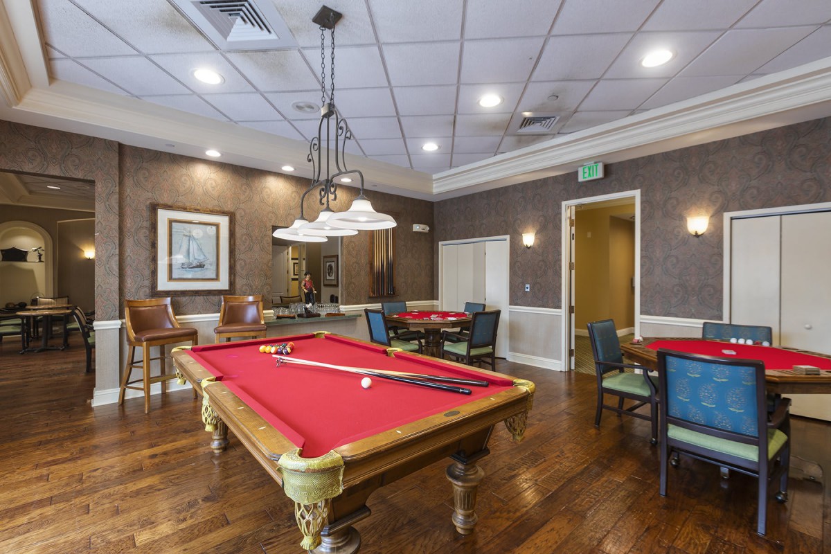 A stylish billiard room featuring a red felt pool table, surrounded by chairs and elegant lighting.