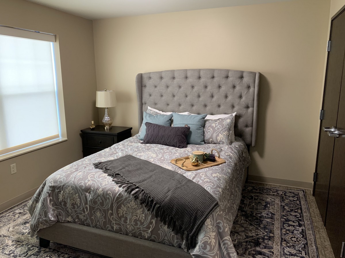 A cozy bedroom with a tufted headboard, neatly arranged pillows, and a bedside lamp.