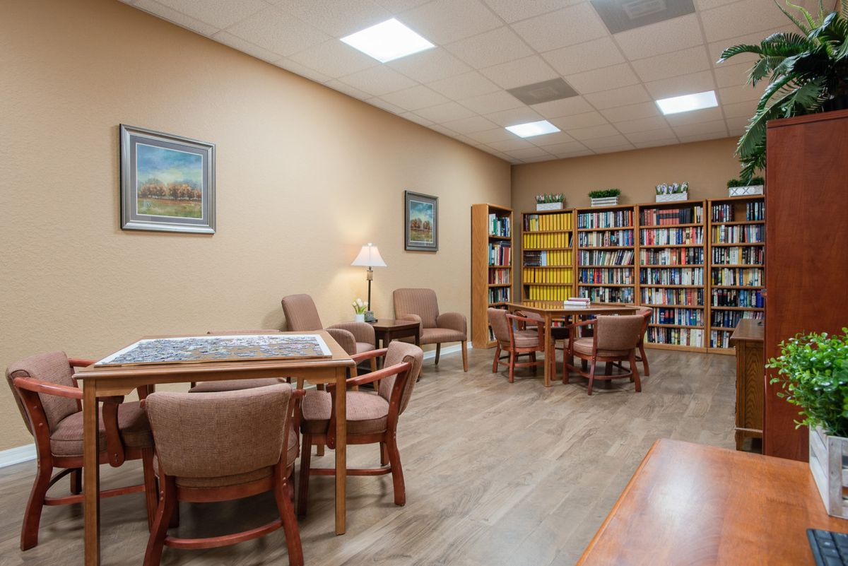 A cozy library reading room with tables, chairs, and bookshelves filled with books.