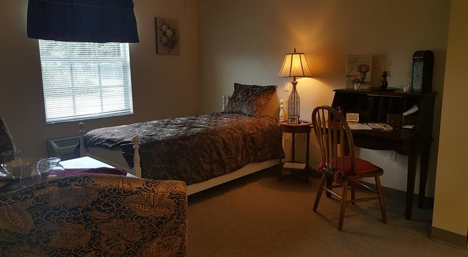 A cozy bedroom with a single bed, lamp, and desk by the window.