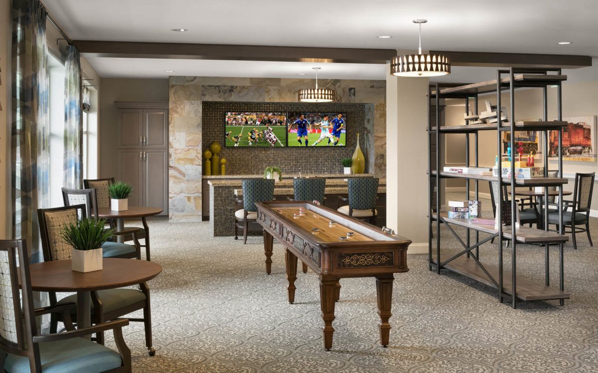 A modern game room featuring a shuffleboard table and a cozy lounge area with bar seating.
