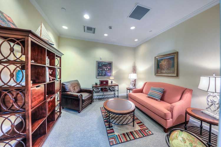 A cozy living room with a pink sofa, armchair, and a wooden coffee table, complemented by a bookshelf and decorative artwork.
