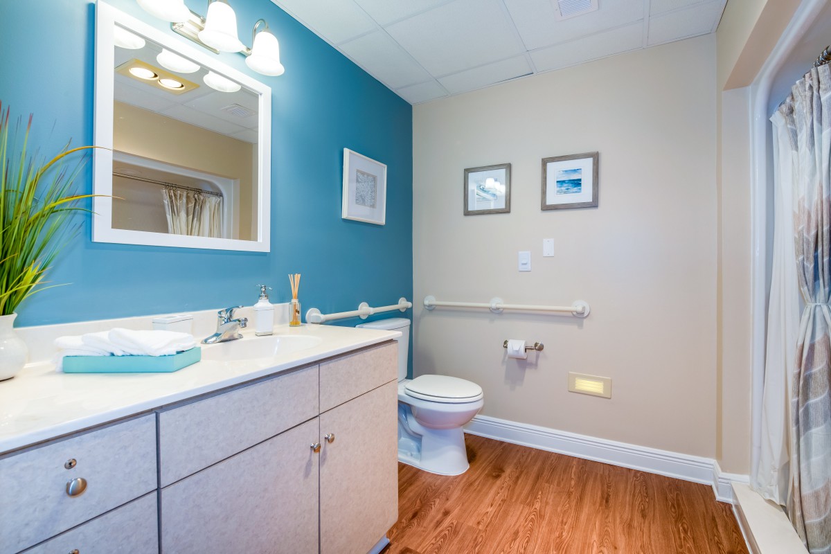 A modern bathroom with a blue accent wall, featuring a sink, mirror, and toilet, complemented by wooden flooring and decorative artwork.