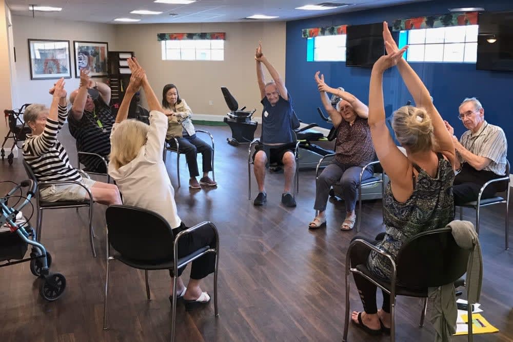 A group of seniors participating in a chair yoga session, led by an instructor in a community center.