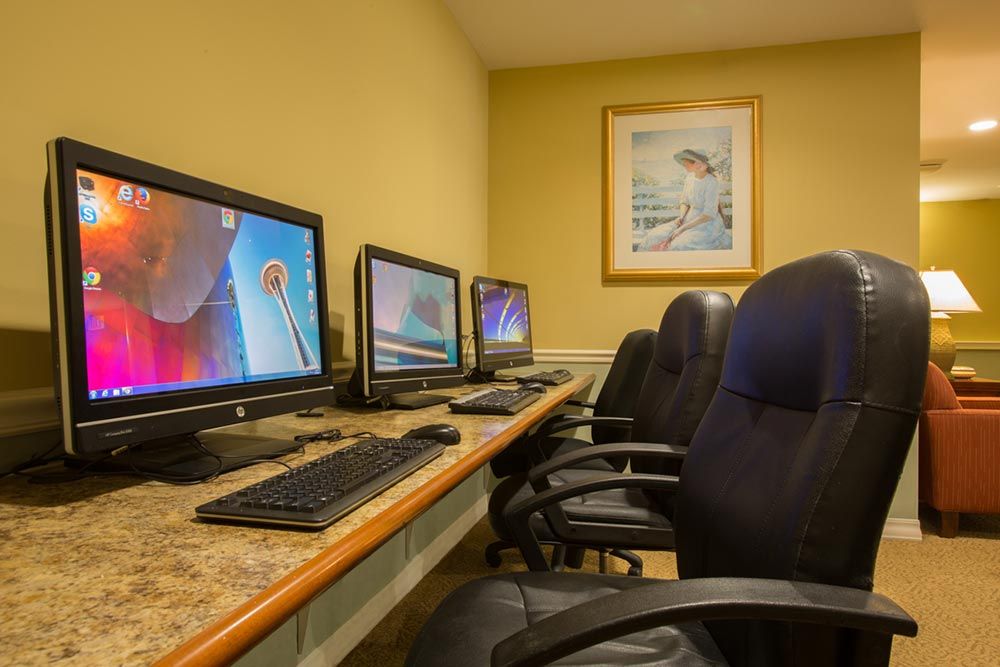 A row of computers on a desk in an office setting with chairs.