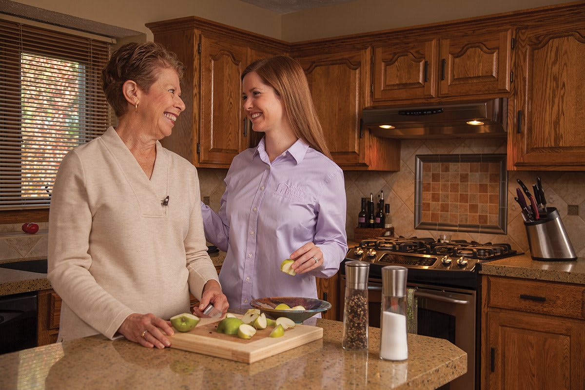 Two women smiling and preparing food together in the kitchen.