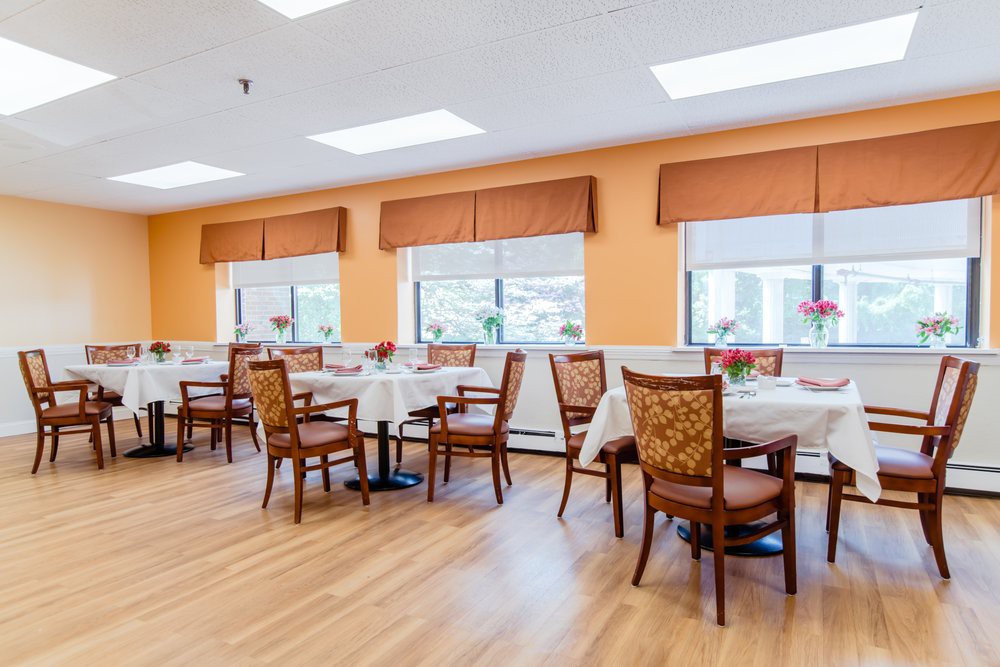 A bright dining room with tables set for a meal and large windows allowing natural light.