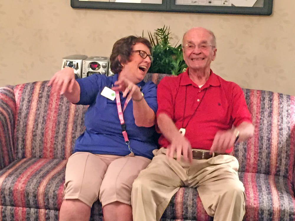 Two elderly people sharing a laugh together on a couch indoors.
