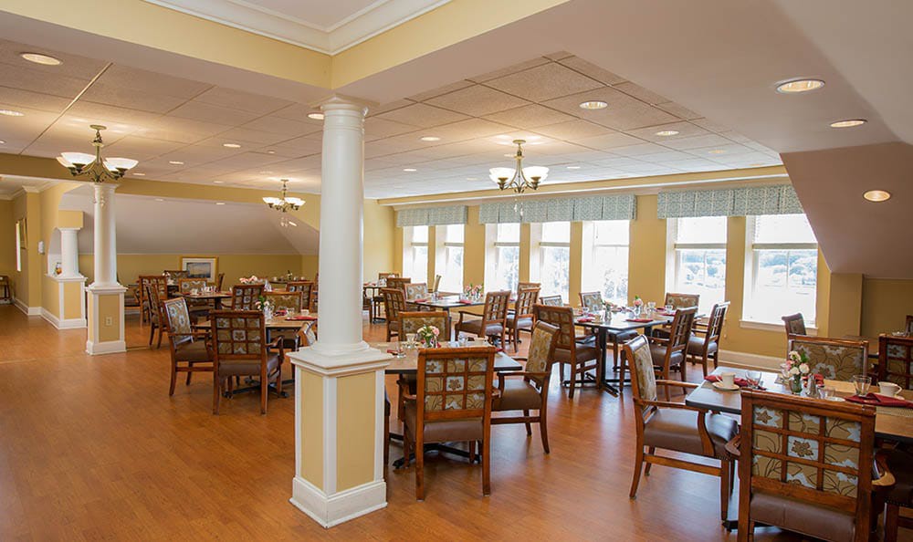 A spacious dining area with neatly arranged tables and chairs, bathed in natural light from large windows.