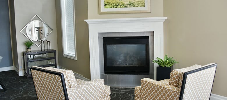 A cozy living room with a fireplace, flanked by patterned chairs and a potted plant.