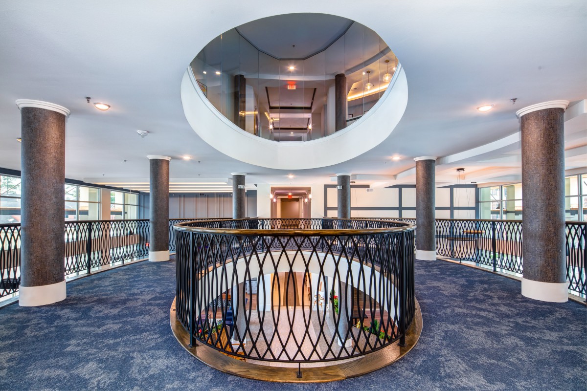 A modern interior with a circular balcony and intricate railing, illuminated by ceiling lights.