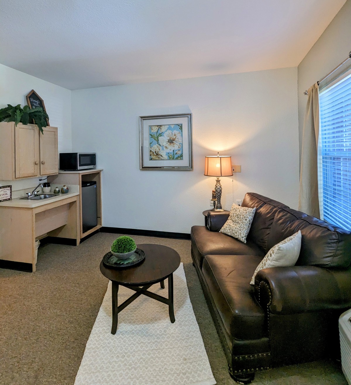 A cozy living room with a leather couch, round coffee table, and a kitchenette in the corner.