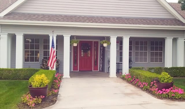 A welcoming house entrance featuring a bold red door, American flag, and colorful flowers.