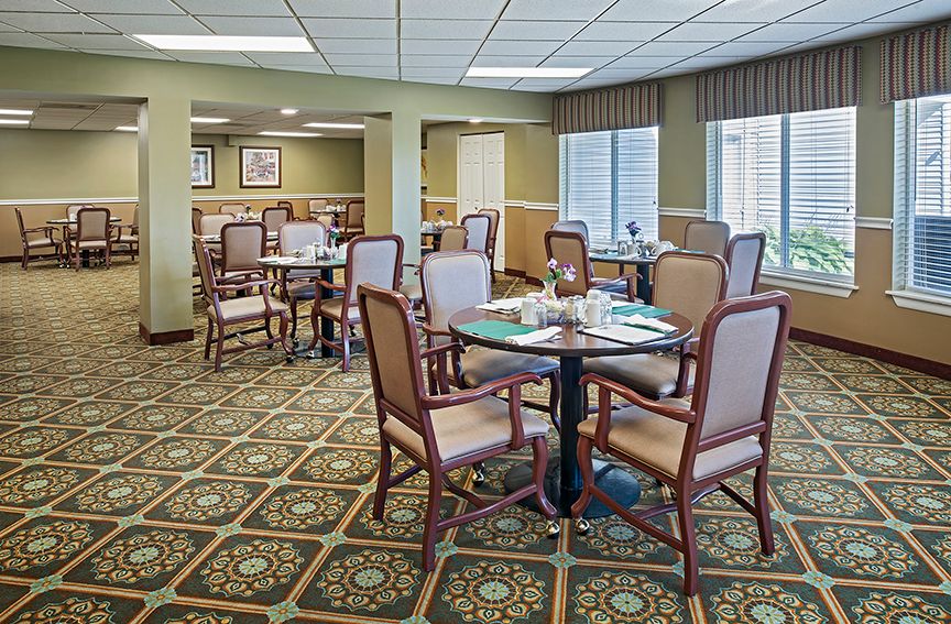 A spacious dining area with neatly arranged tables and chairs, featuring a patterned carpet and soft lighting.