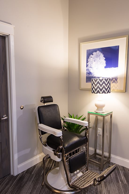 A modern interior featuring a black chair, side table with a lamp, and artwork on the wall.