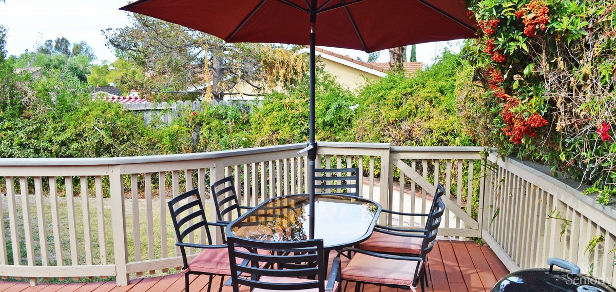 A patio set with a table and chairs under a large umbrella on a wooden deck.