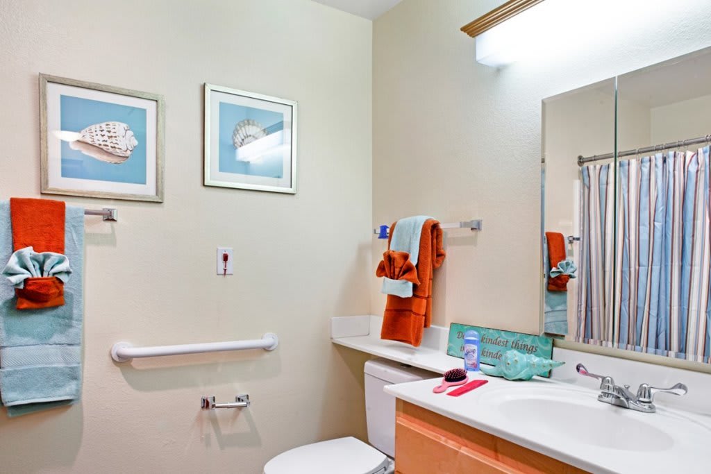 A well-organized bathroom featuring a sink, mirror, colorful towels, and decorative artwork.