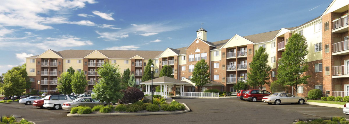 A large, multi-story residential building with landscaped surroundings under a clear blue sky.