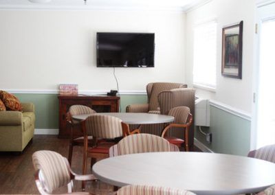 A cozy living room with several chairs and tables, featuring a wall-mounted TV.