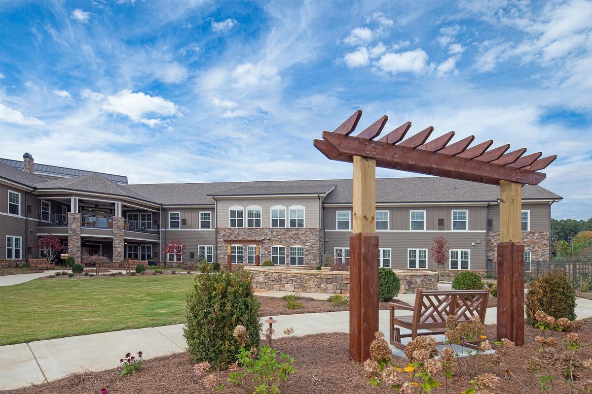 A modern building with a garden and pergola structure under a cloudy sky.