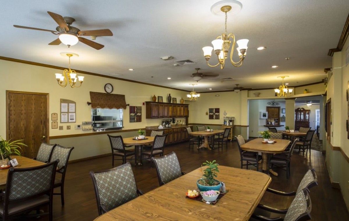 A cozy dining room with wooden tables and chairs, adorned with decorative plants and lit by elegant chandeliers.