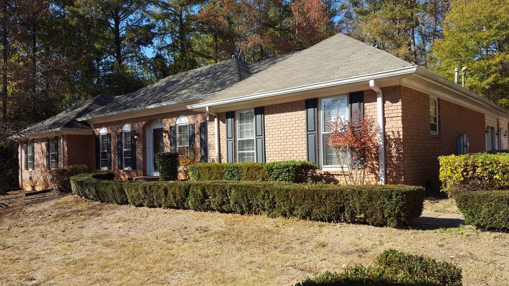 A brick suburban house with a neatly trimmed yard and surrounding trees.