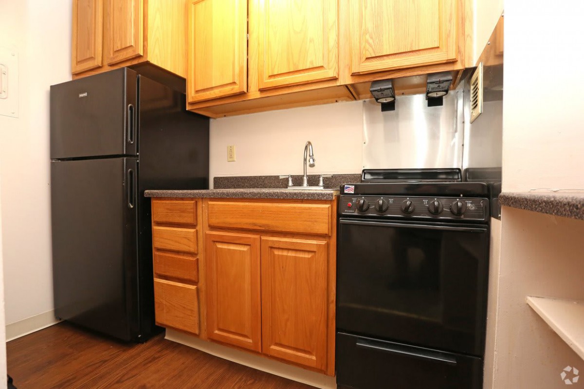 A compact kitchen featuring wooden cabinets, a black refrigerator, and a stove.