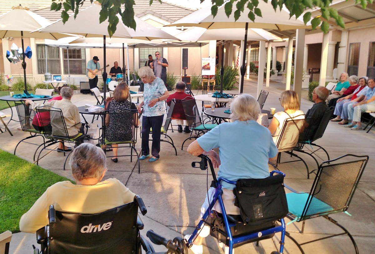 A group of elderly individuals enjoying an outdoor community event under patio umbrellas.