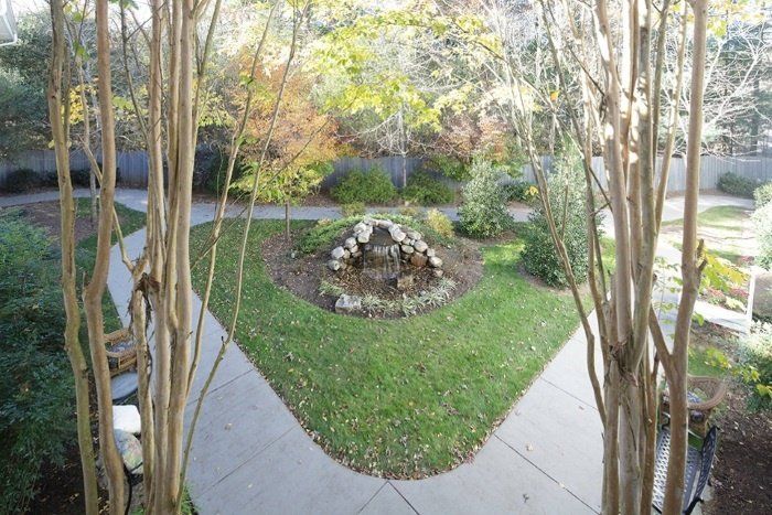 A serene garden with a central stone fountain surrounded by pathways and lush greenery.