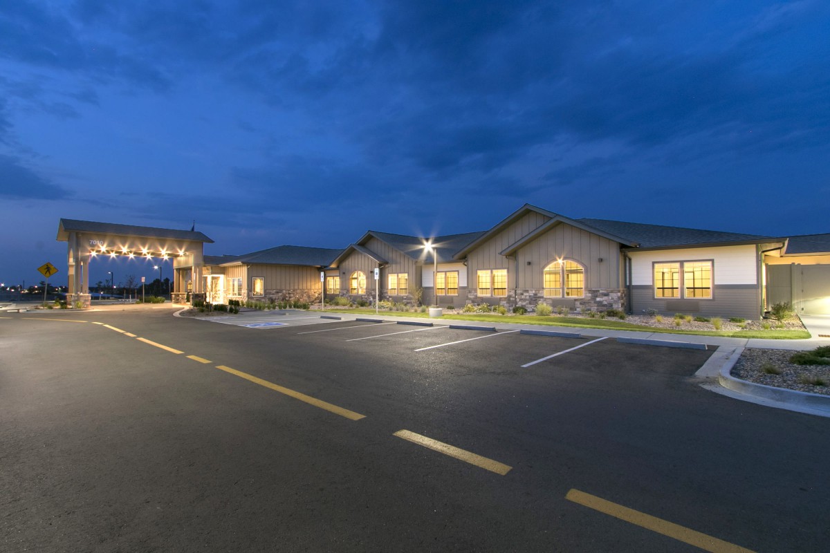 A building with illuminated windows and a parking lot in the evening under a cloudy sky.