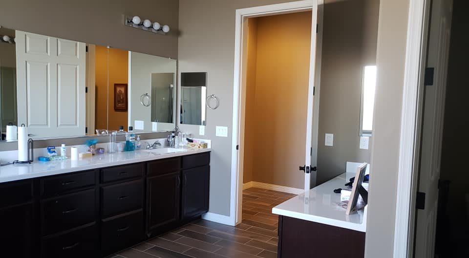 A modern bathroom featuring a large mirror above the vanity with dual sinks and bright lighting.