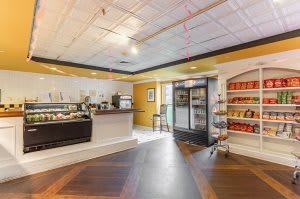 Interior view of a cozy cafe with a service counter, refrigerated drinks, and shelves stocked with products.