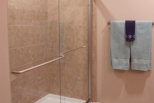 A bathroom with a tiled shower and glass door, featuring towels on the wall.