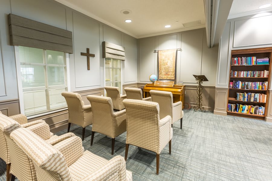 A small chapel room with chairs arranged in rows, featuring a cross on the wall and a podium at the front.