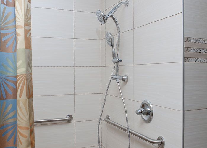 A tiled shower with a handheld showerhead and safety grab bars.