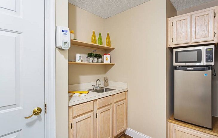 A compact kitchen nook with wooden cabinets, a small sink, and decorative shelves.