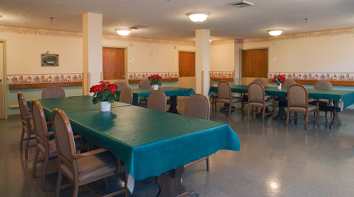 A spacious dining area featuring tables with green tablecloths and decorative flowers, ready for guests.