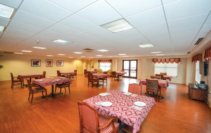 An empty dining hall with neatly arranged tables and chairs on a wooden floor.