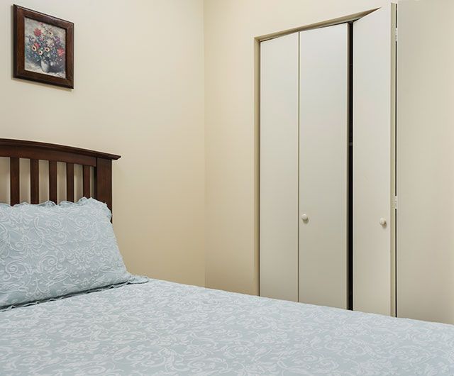 A small bedroom with a bed and closet, featuring a painting on the wall.